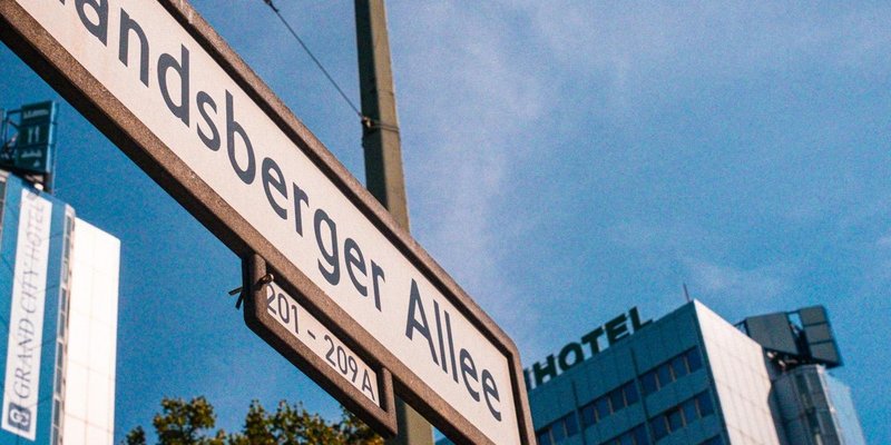 Straßenschild Landsberger Allee, im Hintergrund ein mehrstöckiges Haus mit der Aufschrift Hotel