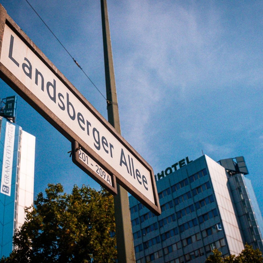 Straßenschild Landsberger Allee, im Hintergrund ein mehrstöckiges Haus mit der Aufschrift Hotel